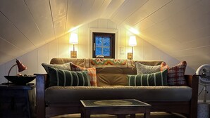 A cozy attic room with a sofa, a small table, and two lamps. - Charming 2-bedroom lake house with AC in Parsonsfield (Parsonsfield)