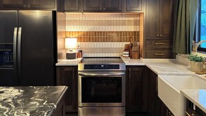 A modern kitchen with dark wooden cabinets, a stainless steel refrigerator, an oven, and a tiled backsplash. - Charming 2-bedroom lake house with AC in Parsonsfield (Parsonsfield)