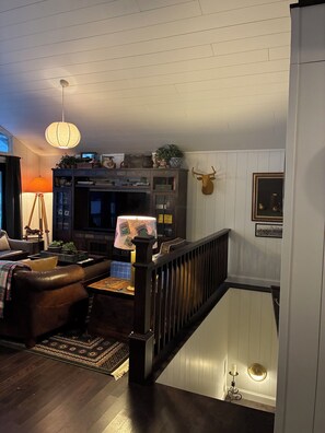 Een gezellige woonkamer met een donkere houten trap, een opgezette hertenkop en een televisie op een houten kast.