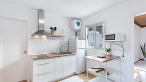 Een moderne keuken met witte kasten, een houten aanrecht, een roestvrijstalen afzuigkap, een ingebouwde magnetron, en een kleine tafel met een plant.