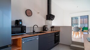Et moderne køkken med opvaskemaskine, mikrobølgeovn, kaffemaskine og ovn. Der er et ur på væggen og et vindue med udsigt til en patio.