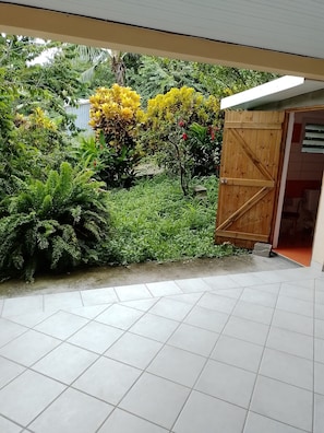 Un jardin avec une porte en bois, une végétation luxuriante et un sol carrelé.
