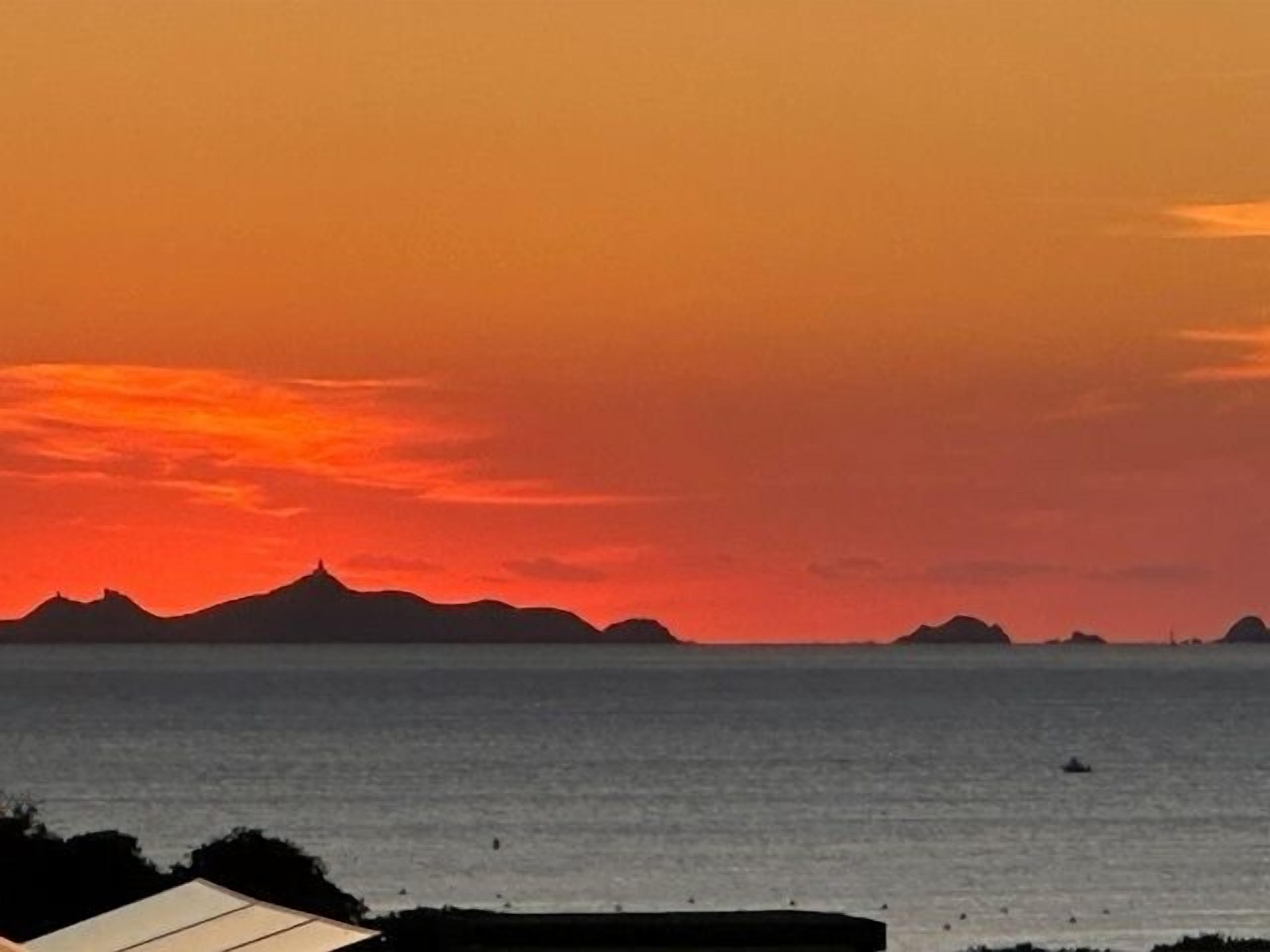 Vista de um pôr do sol à beira-mar, com silhuetas de montanhas e mar calmo.