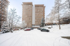 En snötäckt parkeringsplats med bilar och en hög byggnad i bakgrunden.
