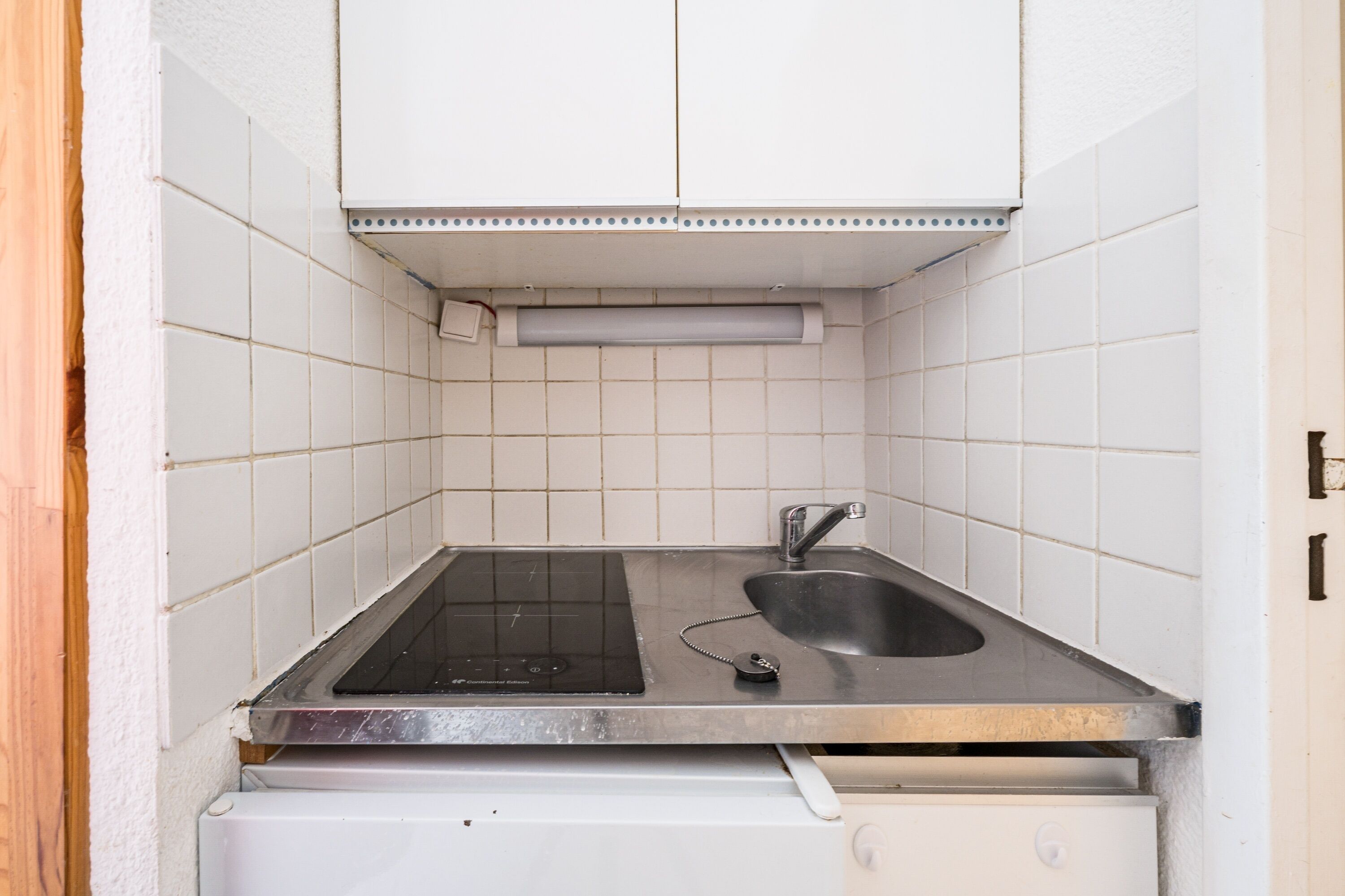 A compact kitchen with a built-in stove, a sink, and a white tiled backsplash.