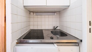 A compact kitchen with a built-in stove, a sink, and a white tiled backsplash. - Le Cocon des Sommets - Studio, station à pied (Villarembert)