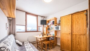 A compact room with a bed, a desk with a chair, a TV, and wooden cabinets. - Le Cocon des Sommets - Studio, station à pied (Villarembert)