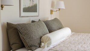 Een net opgemaakt bed met een gewatteerde sprei en twee kussens, een ingelijste foto aan de muur, en wandlampen.