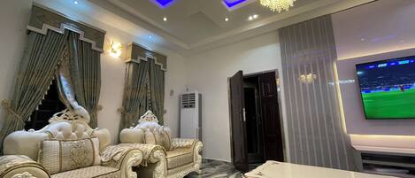 A luxurious living room with ornate sofas, a large TV, and a chandelier.