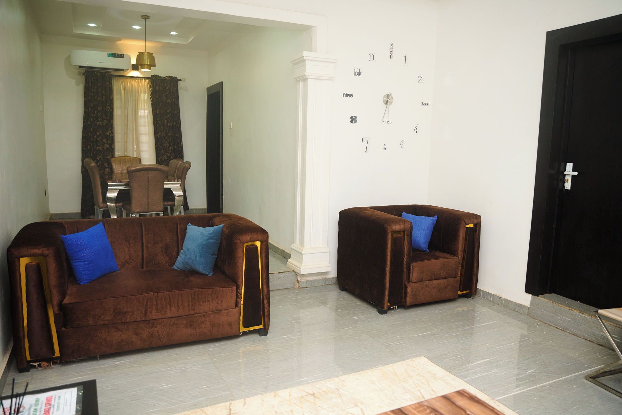 A living room with two brown sofas, a dining area with a table and chairs, and a black door.