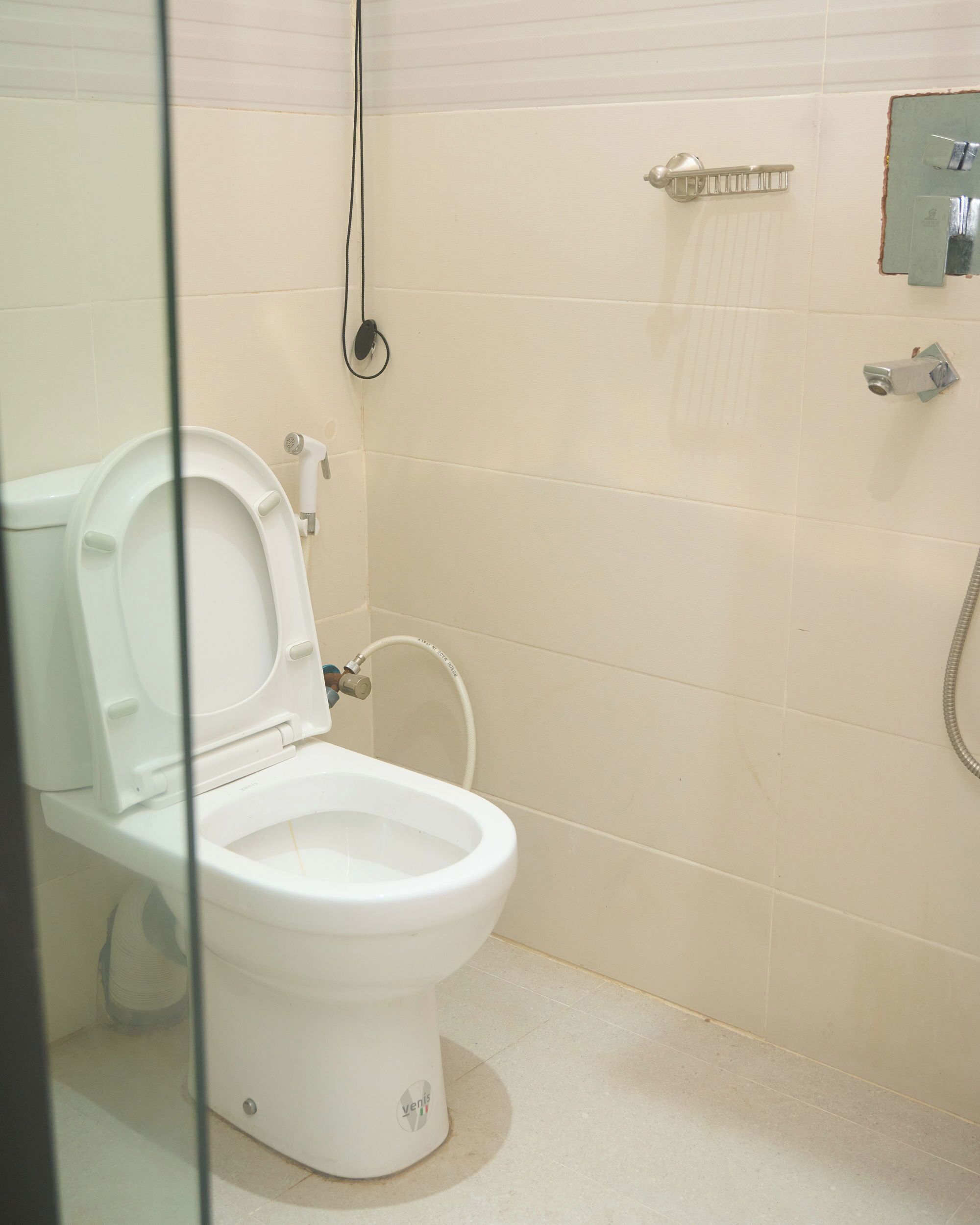Een wit toilet met een bidet, een douchekop en een handdoekhouder in een badkamer met beige tegels.