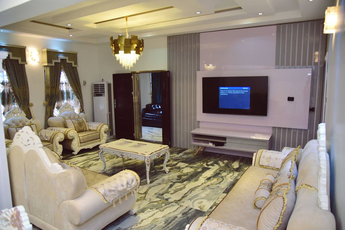 Amplia sala de estar con televisor de pantalla plana grande, elegantes sofás blancos, una mesa de centro y una araña.