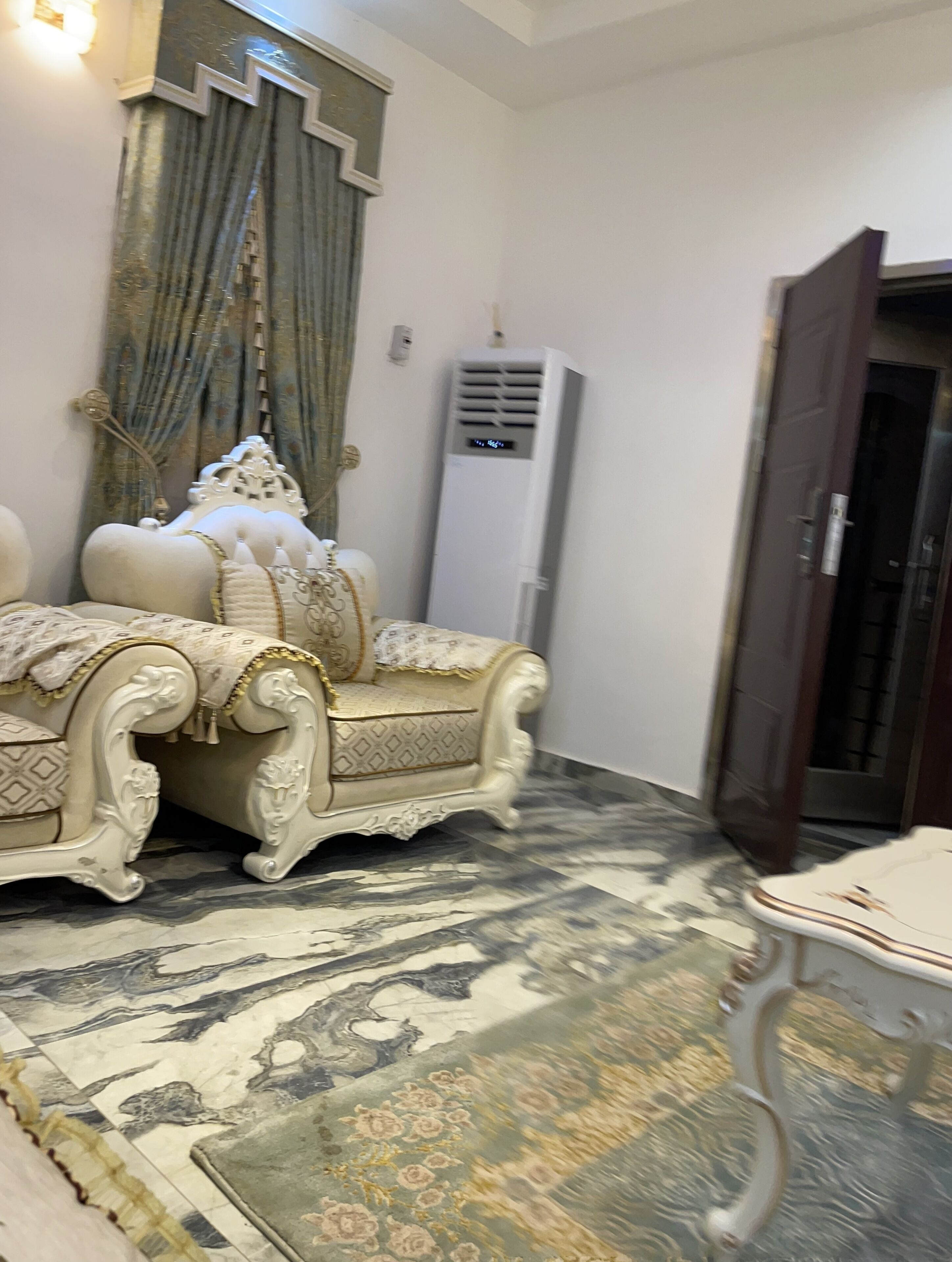 A room with a large ornate sofa, a patterned rug, and a modern air conditioning unit.