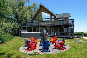 A two-story wooden house with a balcony, surrounded by a grassy lawn and trees. - Large Chalet 10 Bedrooms 14 Beds-Large Hot Tubs-Fire Pit-Projector, Games Room (Blue Mountains)