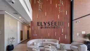 Eine moderne Lobby mit einer gebogenen Couch, runden Tischen und einer Holzwand mit dem Schriftzug "ELYSEE III BY PAN THEON".