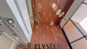 Ein modernes Interieur mit einer vertikalen Holzhakenschrankwand und einem Deckenventilatordesign. Der Text 'ELYSEEL BY PANTHEON' ist sichtbar.