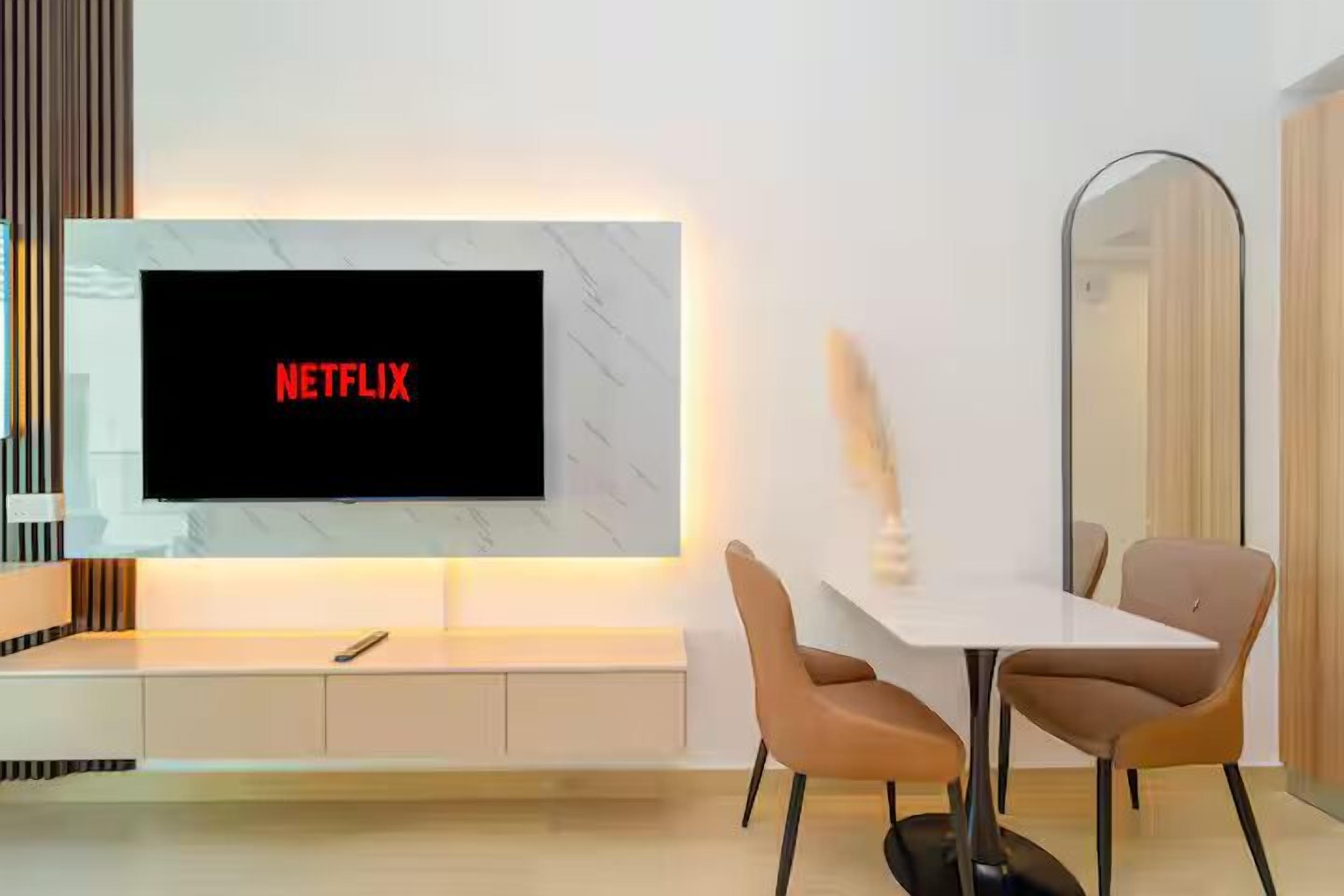Ein modernes Wohnzimmer mit einem flachbildfernseher an einer weißen Wand, einem Esstisch mit zwei Stühlen und einem großen Spiegel.