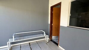 Ein überdachter Patio-Bereich mit einer Metallbank, Fliesenboden und einer Tür zu einem angrenzenden Raum.
