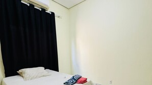 Ein Schlafzimmer mit einem Bett, schwarzen Vorhängen, einer weißen Klimaanlage und Fliesenboden.