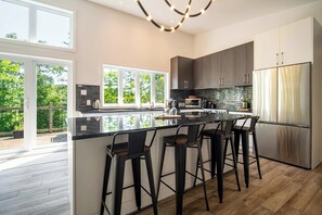 A modern kitchen with a large island, bar stools, and a stainless steel refrigerator.