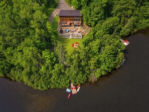 An aerial view of a lodge surrounded by dense forest, with a dock and kayaks visible.