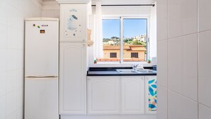 Eine kleine Küche mit Kühlschrank, einem Fenster mit Blick auf Gebäude und einem Spülbecken.