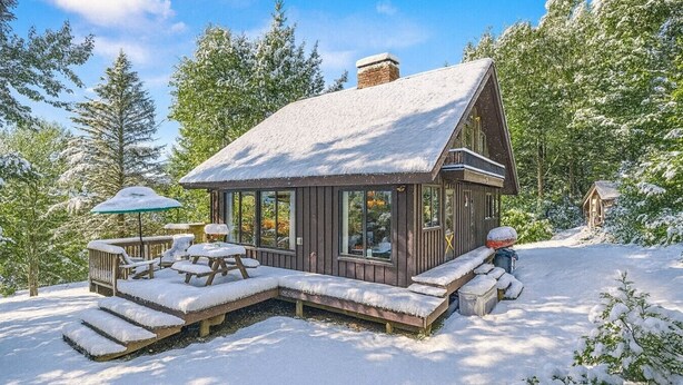 En hytte med snebelagt tag, en terrasse med bænke og en lille veranda.