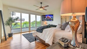Un dormitorio moderno con una cama, un televisor montado en la pared, un ventilador de techo y un ventanal con vistas a zonas verdes.
