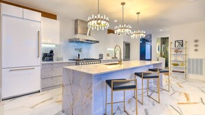 Una cocina moderna con una isla de mármol, taburetes de bar e iluminación colgante.