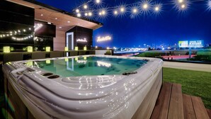 Un jacuzzi con vista a la ciudad de noche, rodeado por una terraza y un edificio moderno.