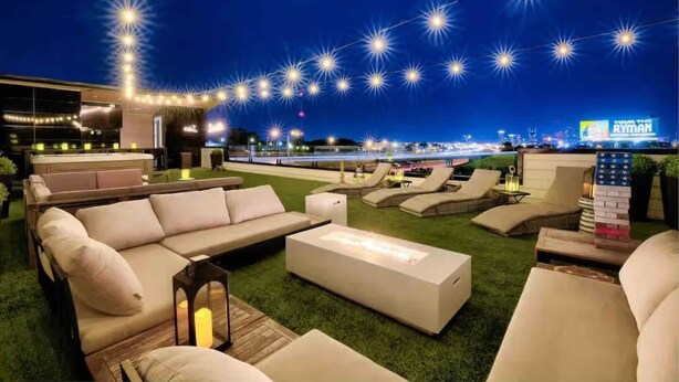Un área de lounge en la azotea con asientos al aire libre, luces colgantes y vistas del horizonte de la ciudad.