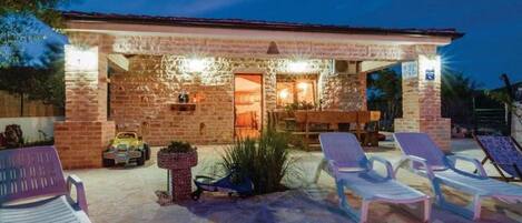 A stone building with a covered patio area, outdoor seating, and lounge chairs.