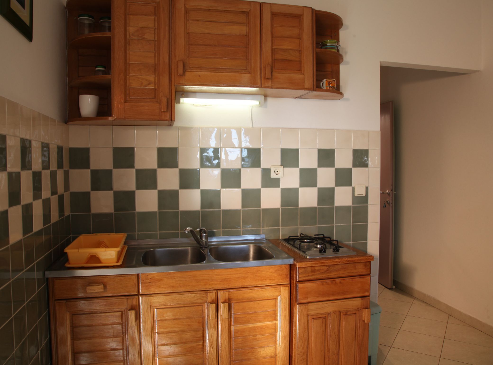 Een keuken met houten kastjes, een gasfornuis, een roestvrijstalen spoelbak en een geruit spatwand.