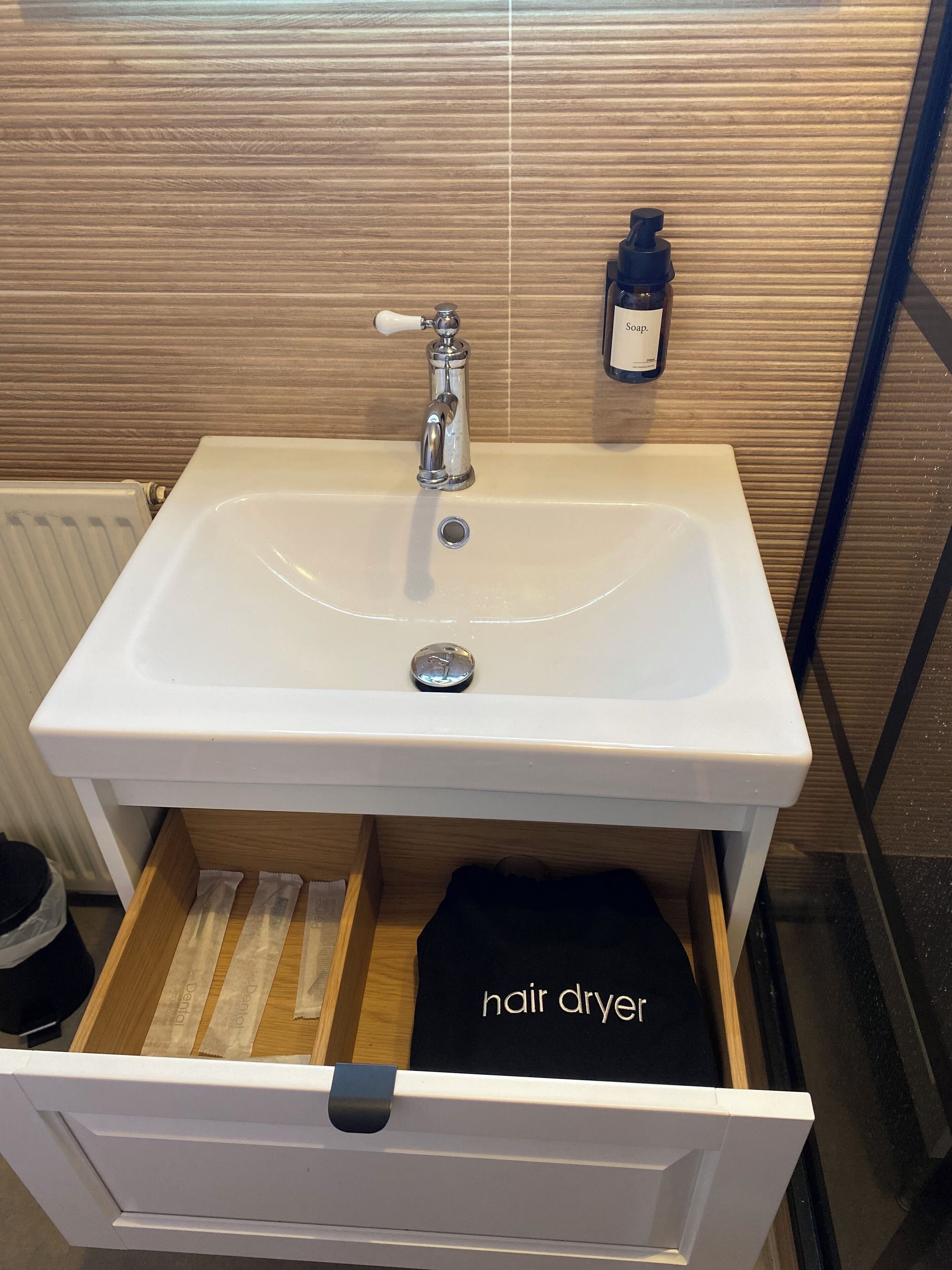 Ein Badezimmer mit einem weißen Waschbecken, einem Haartrockner und einer Seifenfiole.