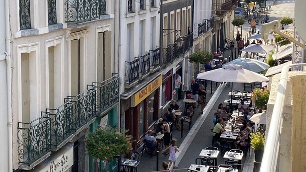 A street view with buildings, outdoor seating, and a mountain in the background. - MAISON GERMÈS - CENTRAL & STANDING (capacity 15 people) - Near Parking (Bagnères-de-Luchon)