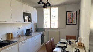 A modern kitchen with white cabinets, a dining area with a table set for two, and a window with a view of the outside. - MAISON GERMÈS - CENTRAL & STANDING (capacity 15 people) - Near Parking (Bagnères-de-Luchon)