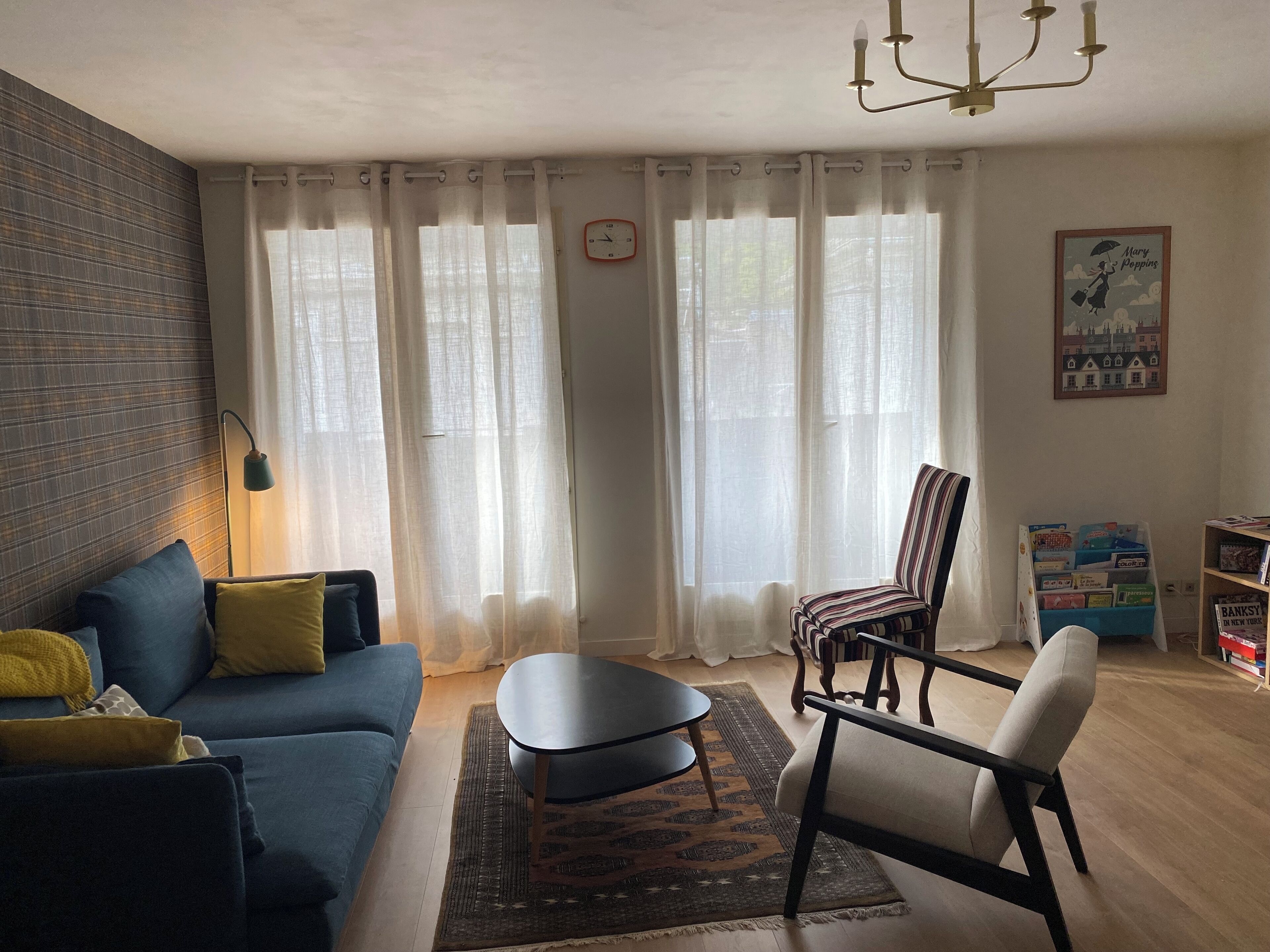 Ein Wohnzimmer mit einem blauen Sofa, einem gestreiften Sessel, einem kleinen Tisch, einem Teppich und einem Bücherregal.