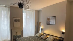 A bedroom with a bed, a bedside table, a mirror, and a wall-mounted light fixture. - MAISON GERMÈS - CENTRAL & STANDING (capacity 15 people) - Near Parking (Bagnères-de-Luchon)