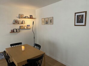 A dining area with a wooden table, black chairs, and a lit candle. There are shelves with framed pictures and a power cord on the wall. - MAISON GERMÈS - CENTRAL & PRESTIGIOUS (Capacity: 15 people) - Near parking (Bagnères-de-Luchon)