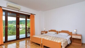 A bedroom with a wooden bed, two bedside tables, an air conditioner, and a balcony with orange curtains. - Sobe Melada (Trilj)