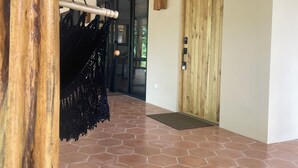 Un pasillo con techo de madera, una hamaca negra, una puerta de madera y suelo de baldosas hexagonales.