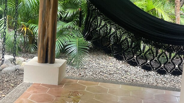 Una hamaca bajo una pérgola de madera en un jardín con baldosas hexagonales y plantas tropicales.
