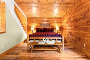 Une chambre dans une cabane en bois, avec un lit, deux lampes de chevet, un banc en bois avec des serviettes et un plafond en bois.
