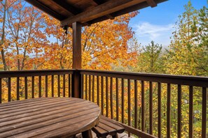 Une terrasse en bois avec une table ronde et des bancs, donnant sur une forêt aux couleurs automnales.