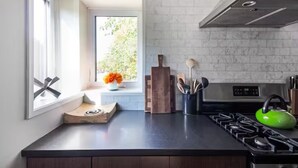 Cocina moderna con estufa a gas, un hervidor verde y una ventana con vistas a zonas verdes.