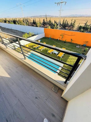 Un área de piscina en la azotea con sillas reclinables amarillas y una vista despejada del paisaje circundante.
