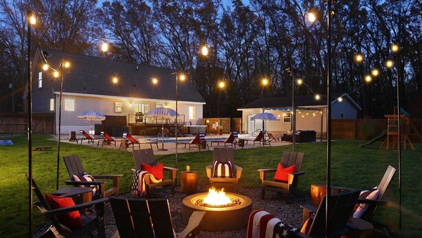 An outdoor patio area with a fire pit, lounge chairs, and string lights. - Pine & Paddle Getaway • Game Room • Hot Tub • Pool (Muskegon)