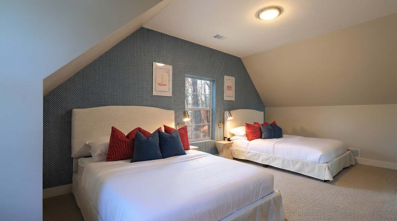 Une chambre avec deux lits, un plafond en pente et une grande fenêtre.