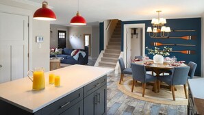 A modern kitchen with a central island, a dining area with a round table, and a staircase leading to another level. - Pine & Paddle Getaway • Game Room • Hot Tub • Pool (Muskegon)