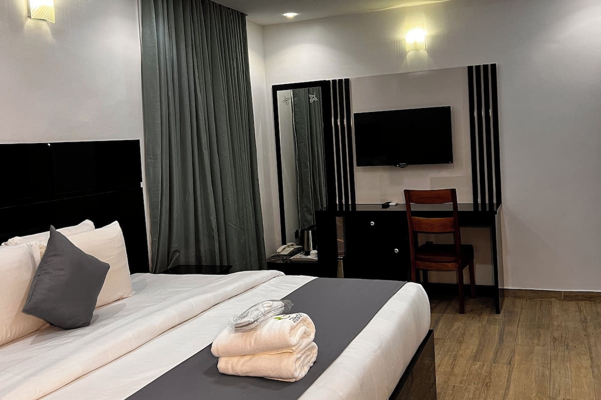 A modern hotel room with a large bed, a desk, a chair, and a flat-screen TV.
